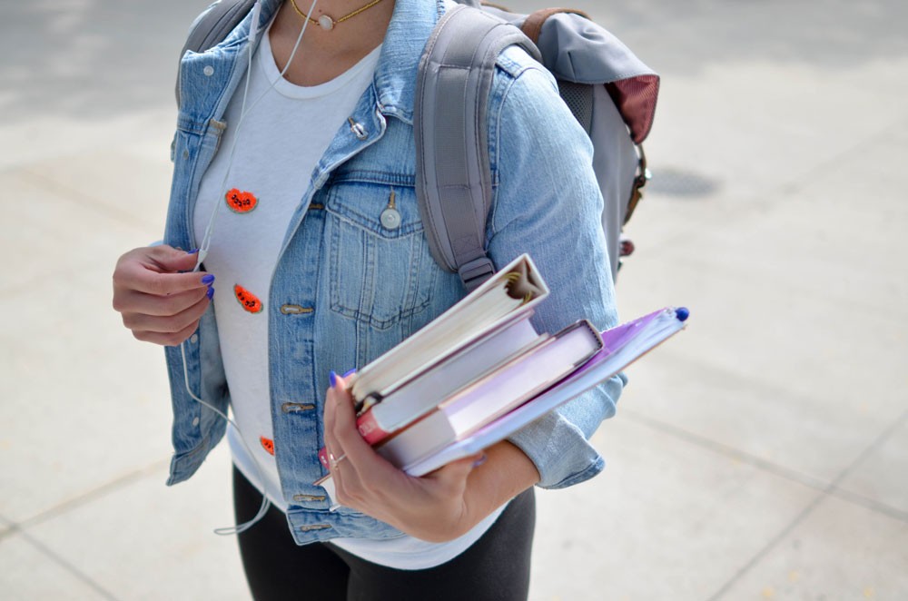 chica con una chaqueta tejana y una mochila sujetando libros con su brazo izquierdo